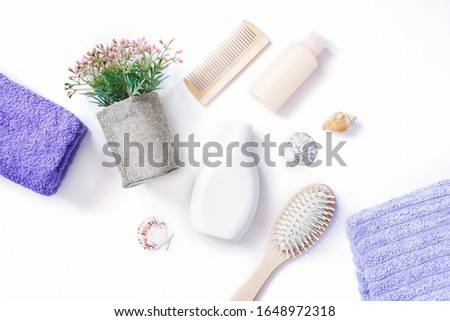 Flat lay photo purple towels, wooden hair brushes, moisturizing shampoo, nourishing balm, flowers and seashells on white background