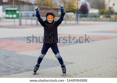 Cute school kid boy skating with rollers in the city. Happy healthy child in protection safety clothes skating with rollers. Active schoolboy making sports and learning to skate on inline skater.