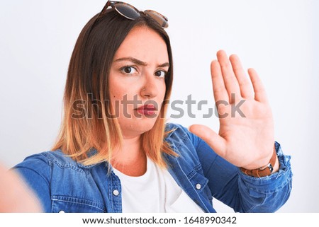 Young beautiful woman wearing denim shirt  standing over isolated white background with open hand doing stop sign with serious and confident expression, defense gesture