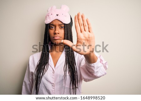 Young african american woman wearing pink pajama and sleep mask over isolated background doing stop sing with palm of the hand. Warning expression with negative and serious gesture on the face.