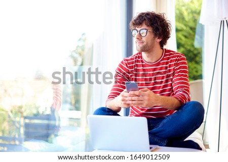 Happy handsome man text messaging and usin laptop while relaxing at home.  Royalty-Free Stock Photo #1649012509