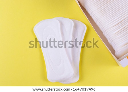 Three sanitary pads and an open pack on a yellow background.
