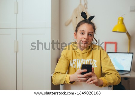 young girl, preteen, sitting desk in her room and using mobile phone