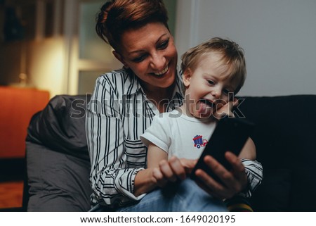 mid aged woman with her son relaxed on sofa using mobile phone at her home