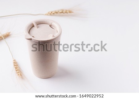 Reusable cup on a white background next to the spikelets of wheat. copy space