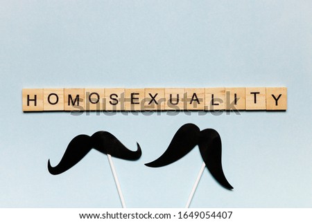 Concept of relations between of men, flatlay overhead black paper photo stand props mustache, homosexuality letter on blue shiny background.
