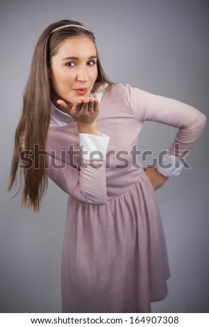 Relaxed pretty model with pink dress on kissing at camera on grey background