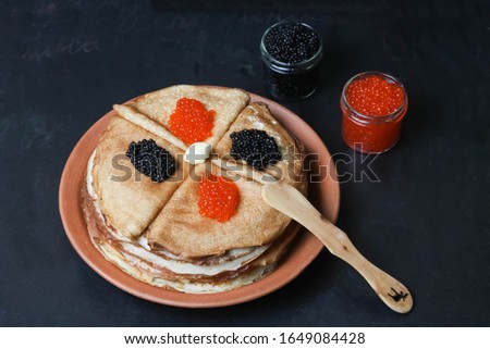 Stack Of Crepes Or Pancakes With Red And Black Caviar On Clay Plate With Wooden Knife, Piece Of Butter And Glass Jar On Black Background. Top View, Flat Lay.
