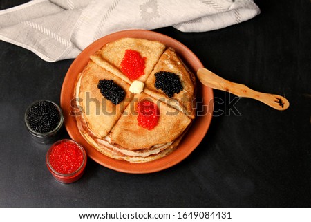 Stack Of Crepes Or Pancakes With Red And Black Caviar On Clay Plate With Wooden Knife, Piece Of Butter And Glass Jar On Black Background. Top View, Flat Lay.