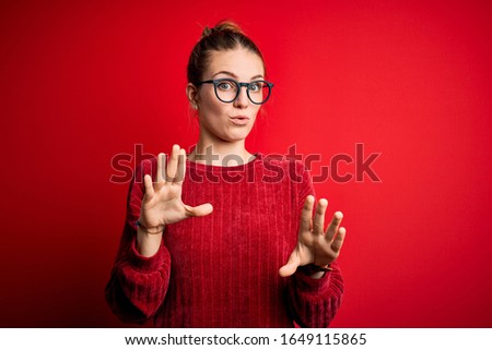 Young beautiful redhead woman wearing casual sweater over isolated red background Moving away hands palms showing refusal and denial with afraid and disgusting expression. Stop and forbidden.