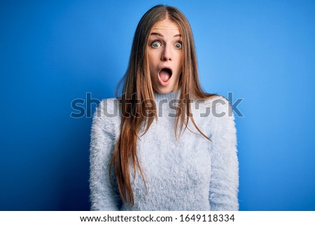 Young beautiful redhead woman wearing casual sweater over isolated blue background afraid and shocked with surprise and amazed expression, fear and excited face.