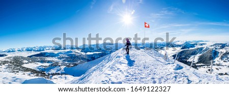winter sports: snow shoe hiker a the top of the snowy mountain in the swiss alps. panoramic picture of winter hiker at the top of the hill in switzerland. mountain panorama with sun and blue sky