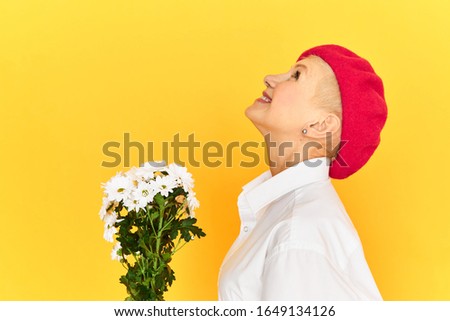 Profile image of stylish mature blonde lady in red bonnet being in good mood smiling broadly with excitement, feeling happy and free, receiving cute bouquet of white dandelion flowers on birthday