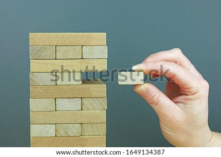 A Hand Holding And Adding A Wooden Block To A Tower. Completing A Project Concept.