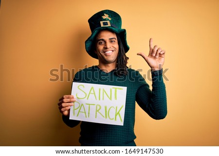 Young african american man wearing green hat holding banner celebrating saint patricks day surprised with an idea or question pointing finger with happy face, number one