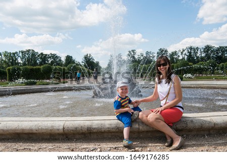 Young woman with her son next to the fountain. Sunny summer day.