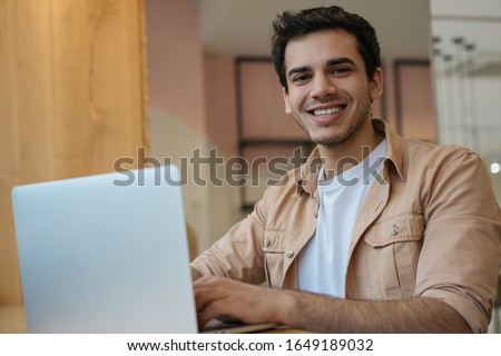 Asian student studying, learning language, online education concept. Portrait of handsome Indian businessman using laptop computer, working in office. Copywriter typing on keyboard, looking at camera