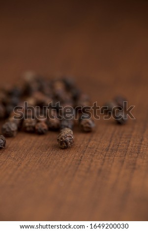 Close up of black pepper or peppercorns on a wooden background.