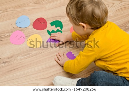 Different color paper eggs on the floor. Easter theme game, find other side of figure. boy playing on the floor.