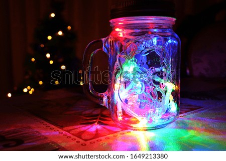 Glass jar with colored lights and Christmas pine in the background. colorful garland. end of year party