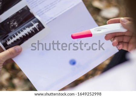 Young woman's hand holding pregnancy test and ultrasound
