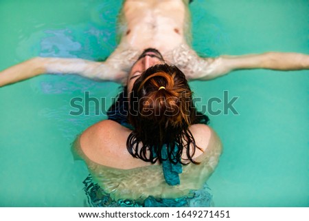 Close-up of young man with closed eyes wearing rubber neck pillow around his neck getting spa water massage treatment. from trainer in swimming pool Royalty-Free Stock Photo #1649271451