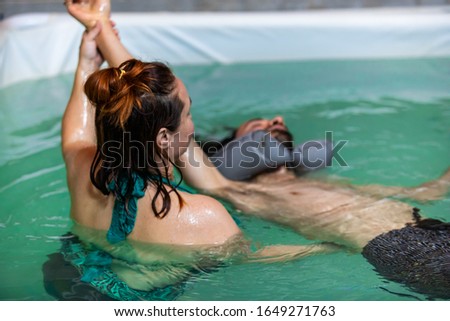 Female therapist giving hand water massage in swimming pool to relaxed young man lying on water in swimming costume during aqua treatment Royalty-Free Stock Photo #1649271763