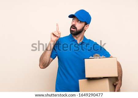 Delivery man with beard over isolated background thinking an idea pointing the finger up