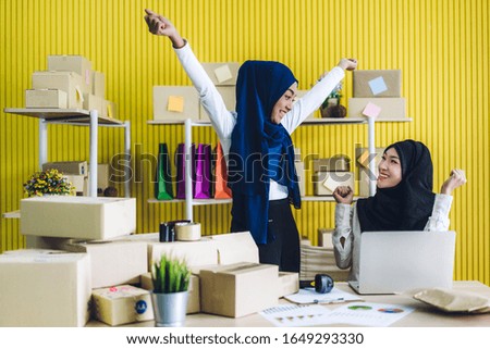 Muslim two asian woman freelancer sme business online shopping working on laptop computer with cardboard box on table at home - Business online shipping and delivery concept