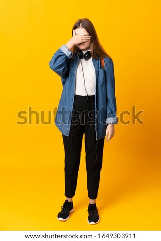 Student ukrainian teenager girl over isolated yellow background covering eyes by hands
