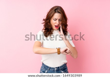 Young Russian woman over isolated pink background with wrist watch and surprised