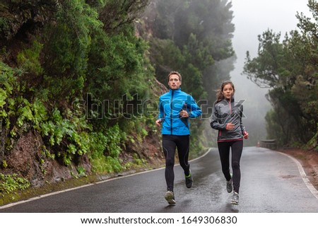 Rain run fit people training jogging in rain weather wearing cold clothing running outdoors in nature autumn season. Active couple on wet park trail jogging. Asian woman, Caucasian man athletes. Royalty-Free Stock Photo #1649306830