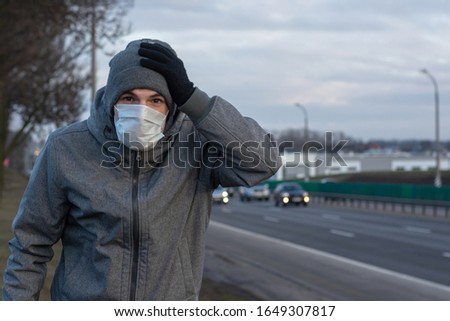 a man is standing on the side of the road where cars are traveling. on the face a protective medical mask. means of protection against viruses, coronovirus, diseases transmitted by airborne droplets.
 Royalty-Free Stock Photo #1649307817