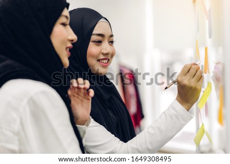 Two muslim business woman planning and brainstorm writing over the project with stickers note on glass window at modern office.Teamwork concept