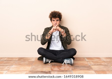 Young caucasian man sitting on the floor showing a sign of silence gesture