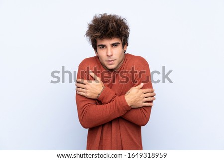 Young caucasian man over isolated blue background freezing