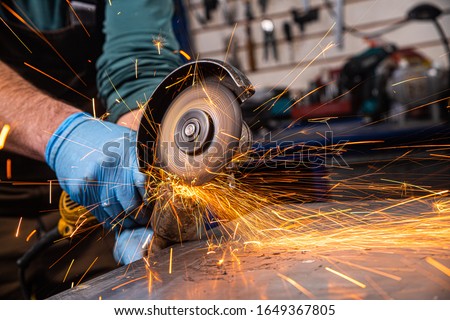 A close-up of a car mechanic using a metal grinder to cut a car silent block in a vise in an auto repair shop, bright flashes flying in different directions, in the background tools for an auto repair Royalty-Free Stock Photo #1649367805