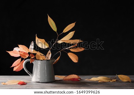 autumn leaves in jug on wooden table on dark background