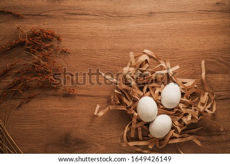 Easter, white eggs on brown paper  and dried plant on wooden table