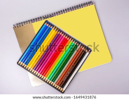 A box with sharpened multi-colored pencils lies on a sketchbook. Items for creativity.