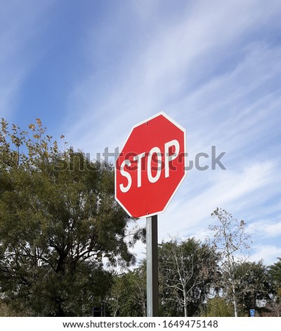 Stop sign against a cloudy blue sky and trees