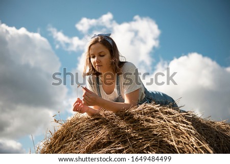 Young woman lying down on a hay bale, looking away and enjoying the sun 