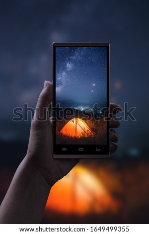 Night shooting on a smartphone. Tent under night starry sky with moon eclipse and milky way on a phone screen.