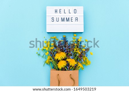 Text Hello Summer on light box and bright bouquet of wildflowers in craft package on blue background. Concept summer time. Top view Flat lay Template for postcard, greeting card.