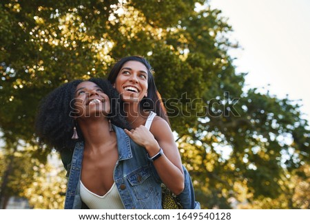 Portrait of a smiling young african american woman giving a piggyback ride to her female best friend in the park on a sunny day - group of college students laughing and having fun on campus Royalty-Free Stock Photo #1649540128