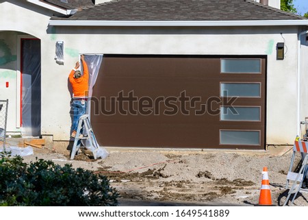 Construction worker putting tape on a door to protect it before putting stucco plaster on the wall. Renovation house concept.