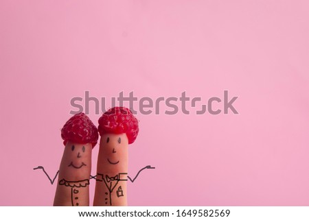 Funny fingers faces in hat raspberries berry against pink background. Happy family couple healthy eating concept.