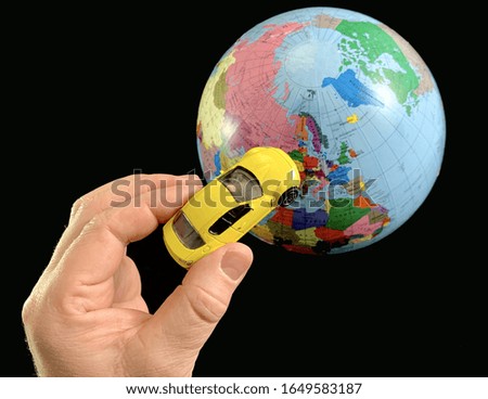 Toy car in hand on a background of the globe. Man with a car model, on a black background. A man points his hand to the globe. Concept: travel, tourism, geography