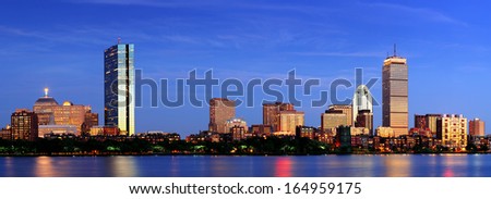 Boston city skyline with Prudential Tower and Hancock Building and urban skyscrapers over Charles River at dusk with lights and water reflection.