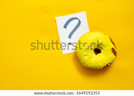 One yellow doughnut on yellow background with a white question mark sheet. Healthy or tasty: donut. Choise. Soft focus. Top view with place for text.
